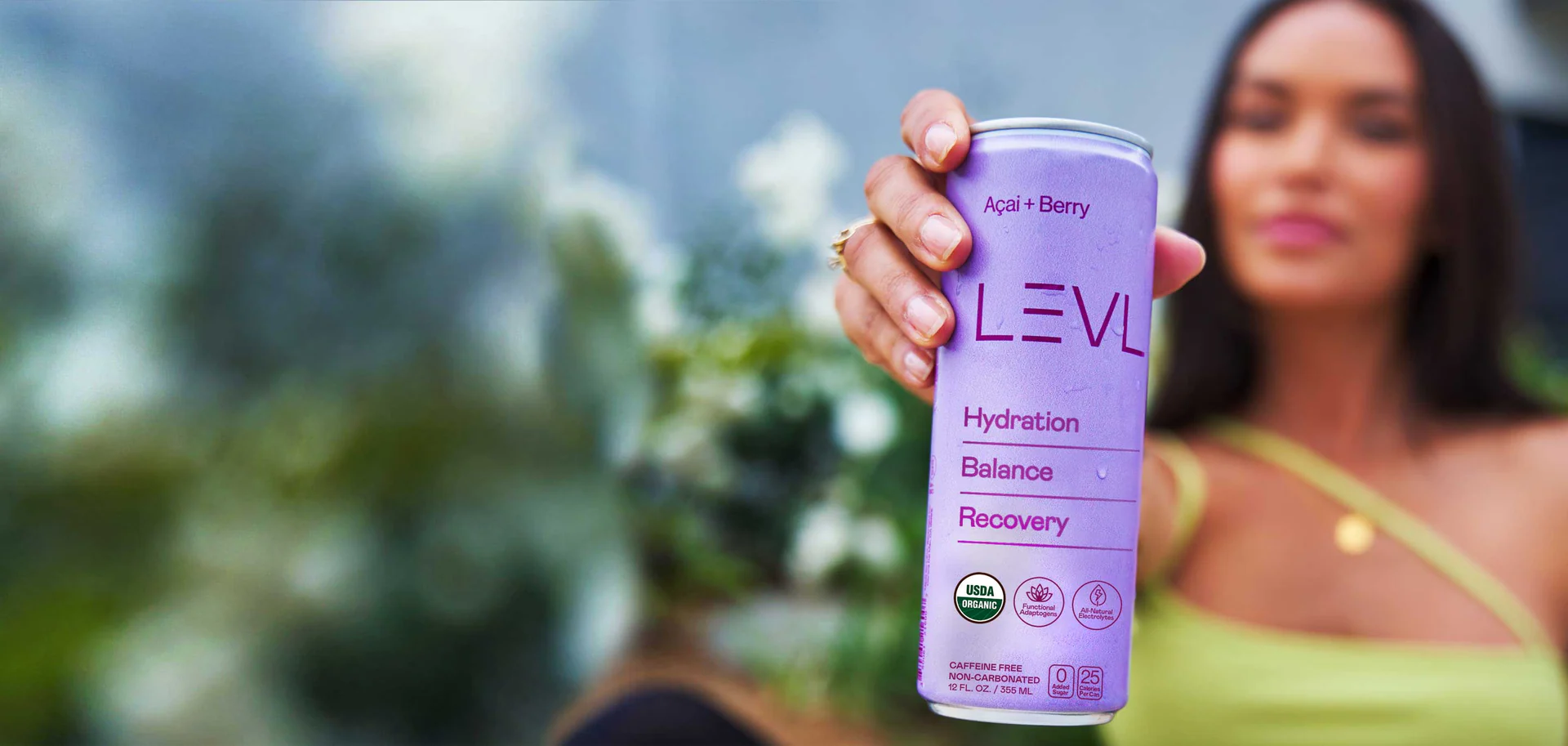 Outdoors, a woman holds a chilled can of LEVL Açaí + Berry out toward the camera