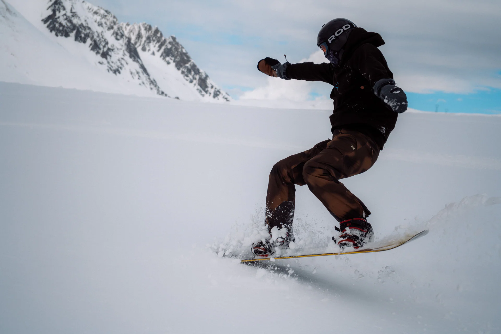 Snowboarder bajando una ladera nevada de alta montaña.